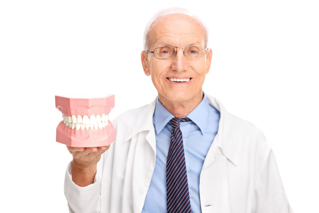 Mature dentist in a white coat holding a denture