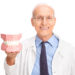 Mature dentist in a white coat holding a denture